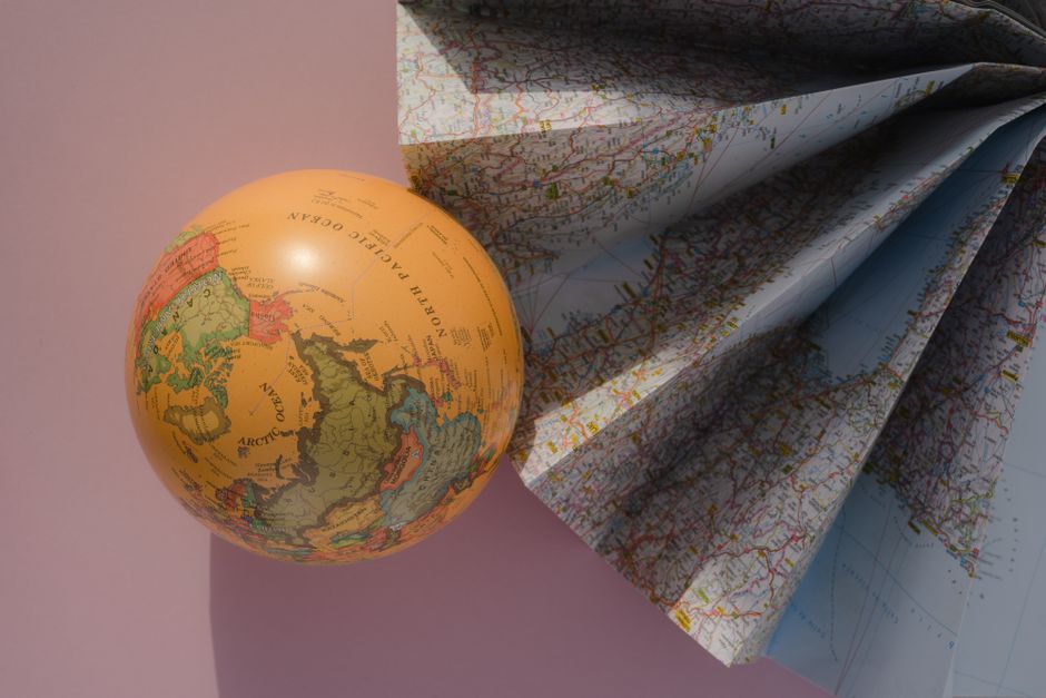 A globe and a folded map on a pink background, showcasing geography and cartography.