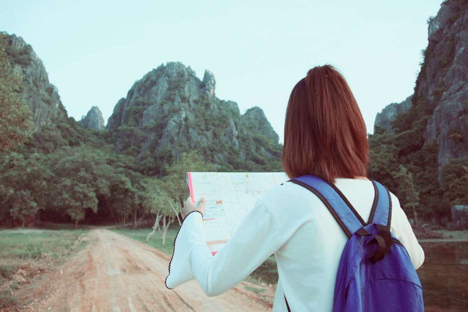 Young woman with a backpack explores nature using a map, surrounded by scenic mountains.